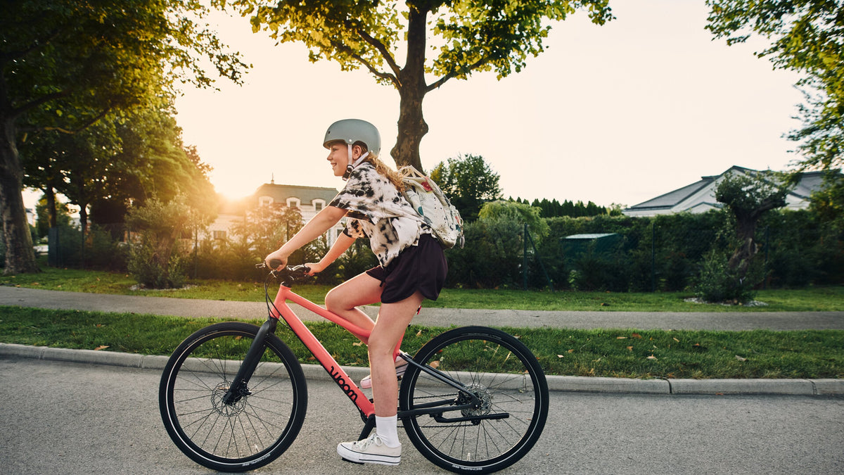 Schülerin fährt bei sonnigem Wetter mit einem Woom Fahrrad auf dem Schulweg